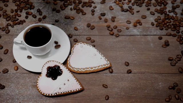 Food art. Good morning concept. cup of coffee and 2 heart-shaped gingersnaps are on wooden background. Coffee beans fall down in slow motion