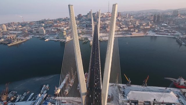 Vladivostok Russia Golden Horn Bay cable-stayed bridge Pylon main Summit urban landscape Road traffic cars impressive Port architecture embankment modern attraction. Winter snow sunset. Aerial Forward