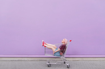 Young model poses with a cart on the background of a purple wall. Stylish girl with a shopping cart on a purple background.