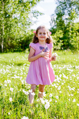 female child in a pink summer dress collects flowers in a clearing