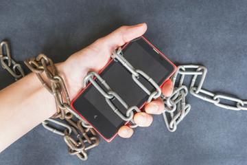 Technology addiction concept, smartphone and chains on the dark background.