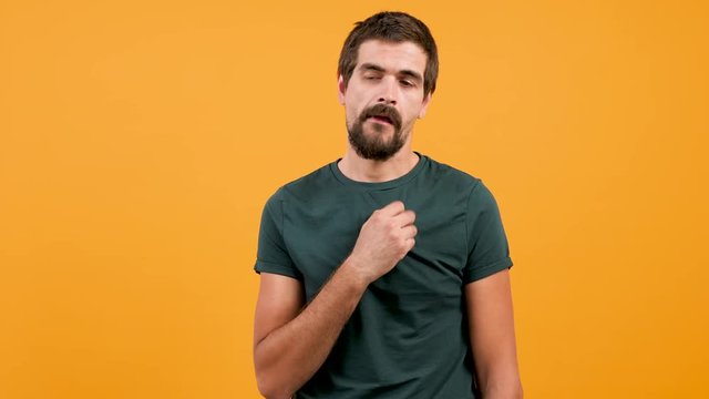 Bored man wearing a casual green t-shirt and chewing gum on yellow orange background