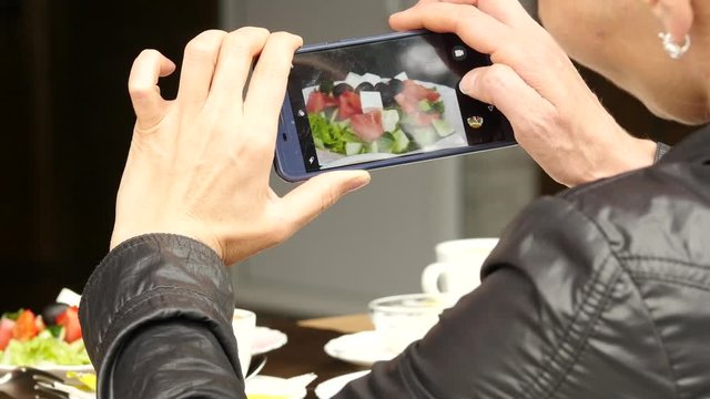 woman in outdoor cafe takes a picture of food green salad and cup of coffee. 4K