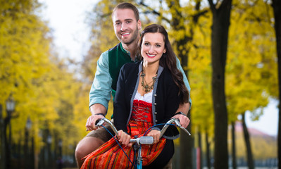 Man and woman in southern German Tracht riding bicycle together laughing