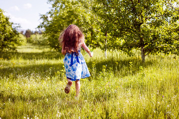 little girl in a dress with blue flowers runs in the meadow and rejoices