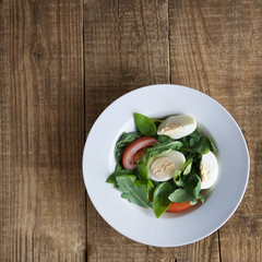 Green health salad with sliced boiled eggs, tomato and fresh lettuce, arugula and spinack served on wooden table. Top view. Square image.