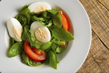 Green health salad with sliced boiled eggs, tomato and fresh lettuce, arugula and spinack served on wooden table. Top view.