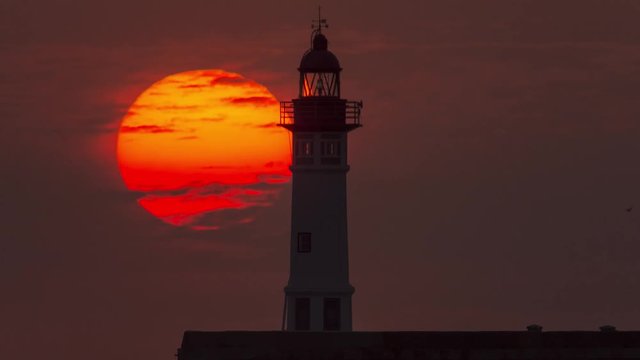 Huge Sun Setting next to a Lighthouse