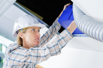 female worker fitting ventilation system in buildings ceiling