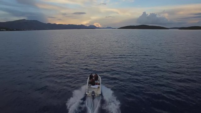 Aerial footage of the boat ride from behind at the sea sunset. Friends on vacation boat ride.