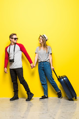 Happy teen couple with suitcases and camera on yellow background