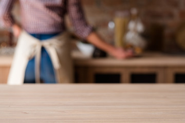 home kitchen workspace. woman cooking in the background. selective focus on the empty wooden table...