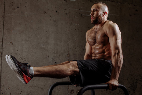 powerful fit shirtless man working out on P bars at gym. side view full length photo. lifestyle and fitness concept