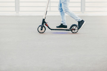 Outdoor shot of man in sneakers and jeans being photographed in motion while rides electric scooter. People and active lifestyle concept