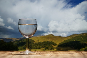 A glass glass glass with clean water stands on a wooden table against a mountain landscape.