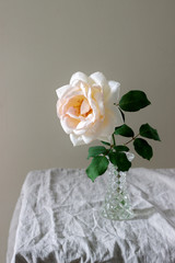 A pink rose in a glass vase on a table with a linen tablecloth. Rustic style.