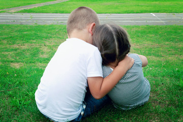 Happy children - boy and girl are sitting on the grass, having fun and embracing. The concept of friendship and family.