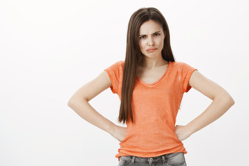 Fototapeta premium How could you forget about my birthday. Portrait of offended upset beautiful woman, holding hands on hips and frowning, looking with contempt and disappointment at camera, standing over gray wall
