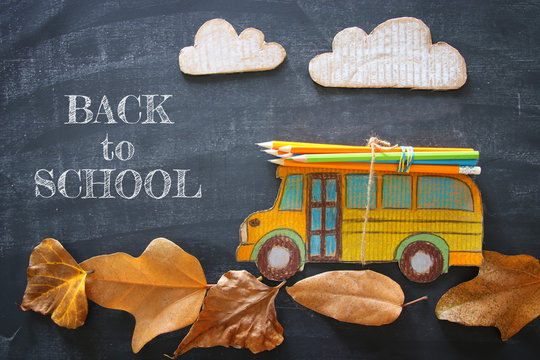 Back to school concept. Top view image of school bus and pencils over autumn dry leaves classroom blackboard background.