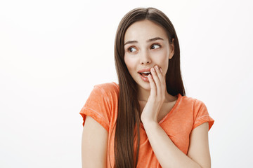 Studio shot of beautiful chatty european girl with dark hair, covering mouth and looking aside while whispering, telling secret or spreading rumor, talking with coworker about recent gossip in office