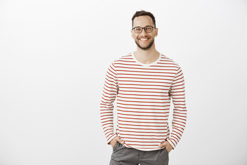 Portrait of confident friendly Caucasian employer in black glasses and striped pullover, holding...