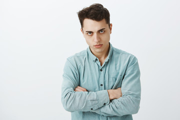 Portrait of offended pissed off european man in shirt, holding hands crossed on chest, looking from under forehead with disdain and offence, standing angry and fed up over gray background