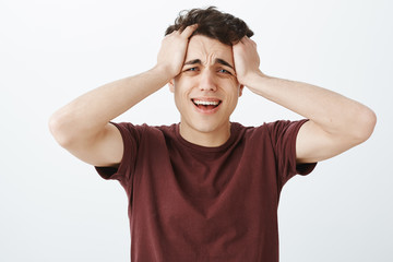 Studio shot of desperate crying caucasian man in red t-shirt, touching hair and screaming or whining, feeling miserable and brokenhearted, standing unhappy over gray background