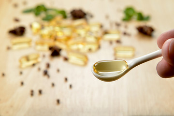 Medicine herb, Cod liver oil omega 3 gel capsules on white spoon over healthy medicinal plant on wooden brown tone background.