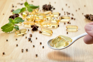 Obraz na płótnie Canvas Medicine herb, Cod liver oil omega 3 gel capsules on white spoon over healthy medicinal plant on wooden brown tone background.
