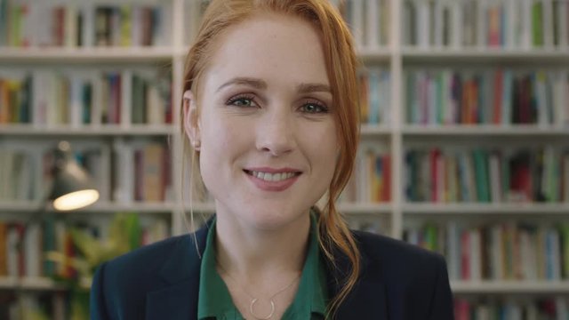 portrait of attractive young red head business woman intern smiling happy enjoying professional career opportunity in library background