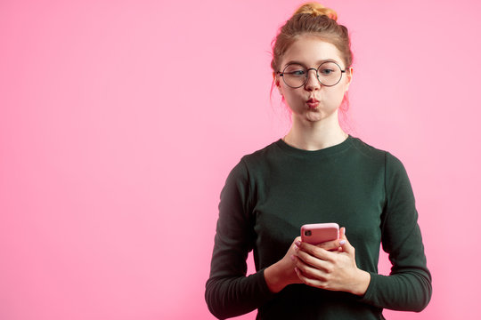 Portrait Of Funny Girl Making Fish Face, Grimacing And Having Fun At Studio, Preparing To Take Selfie Holding Mobile Phone And Isolated Over Pink Background