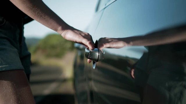 Caucasian female hand opens front door of car by pulling door handle. Clip was shot outside on bright sunny day on side of road. Body of female can be noticed in reflection of vehicle door.