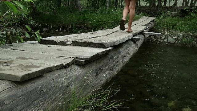 young woman are walking along a narrow wooden bridge over a mountain river. camping and adventure concept