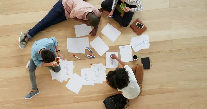 top view young diverse group of multi ethnic web developers brainstorming ideas for startup business website using paper notes planning design layout on wooden workspace floor close up time lapse