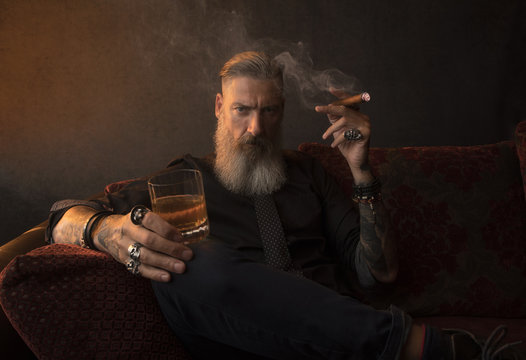Portrait eines attraktiven Geschäftsmannes mit einer Zigarre und einem Glas Whiskey vor dunklem Hintergrund