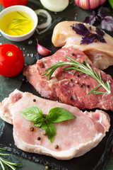 Fresh raw meat. Different types of raw pork meat, chicken fillet and beef with vegetables and herbs close-up on dark wooden background.