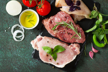 Fresh raw meat. Different types of raw pork meat, chicken fillet and beef with vegetables and herbs on dark wooden background. Top view. Copy space.