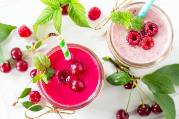 Raspberry and Cherry milkshake or smoothie on a white wooden background. Healthy juicy vitamin drink diet or vegan food concept.