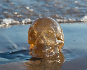 Fototapeta na wymiar Natural Citrine Quartz skull on wet sand on the beach at sunrise. 