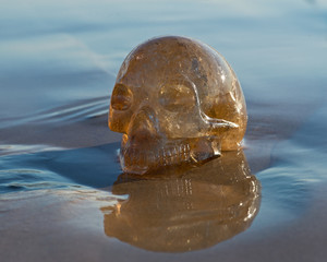 Fototapeta na wymiar Natural Citrine Quartz skull lying on wet sand on the beach at sunrise. 
