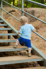 a small curly-headed boy climbs up the stairs. Ladder in the park