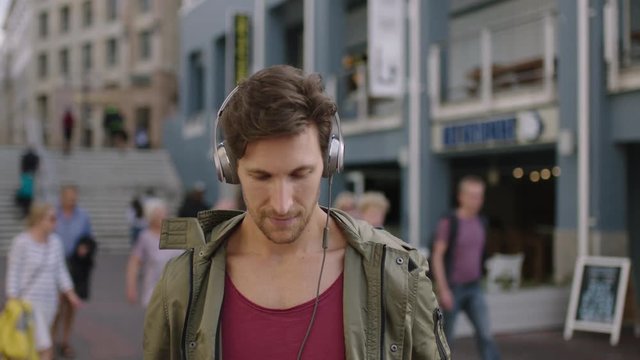 portrait of young attractive caucasian man in busy urban street wearing headphones listening to music enjoying lifestyle