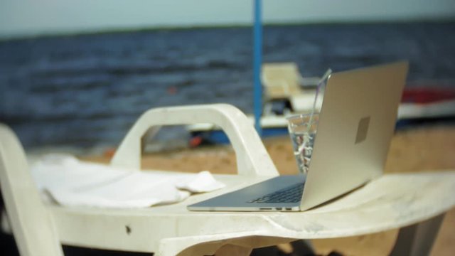 Laptop and a glass of water on a chaise longue overlooking the ocean