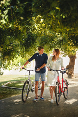 Obraz premium Happy stylish loving couple walking with bicycles in a park