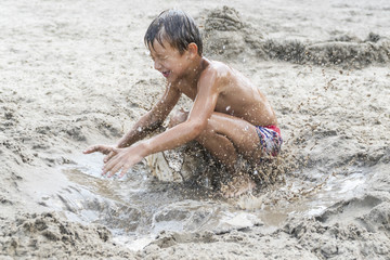 Little boy playing on the beach jumping in the wet dirty sand