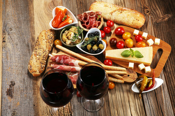 Italian antipasti wine snacks set. Cheese variety, Mediterranean olives, crudo, Prosciutto di Parma, salami and wine in glasses over wooden grunge background.