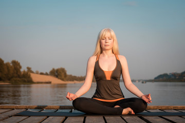 a woman practicing yoga. healthy lifestyle. yoga on the river pier. healthy lifestyle. a woman with blond hair meditates on the background of the river and the sky.