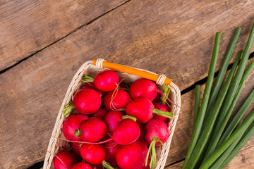 Gathered radish in a wicked basket and green onion. Top view. Wooden desk table background.