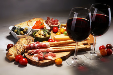 Italian antipasti wine snacks set. Cheese variety, Mediterranean olives, crudo, Prosciutto di Parma, salami and wine in glasses over stone grunge background.