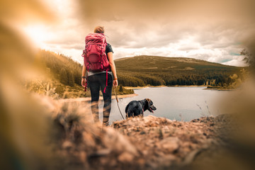 young woman with backpack and german shepherd dog puppy standing on mountain in front of forest and...